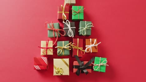 Video-of-christmas-gifts-forming-christmas-tree-and-copy-space-on-red-background