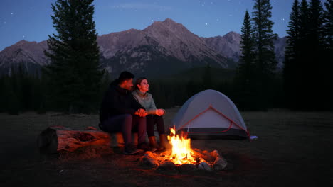 couple camping by the campfire under the stars in the mountains