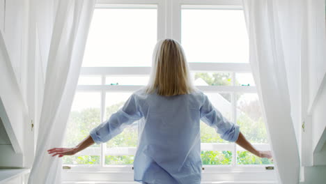 rear view of woman opening curtains and looking out of window