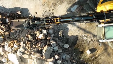 top-down view of an excavator's arm gathering rubble and debris on a construction site, showcasing heavy machinery in action