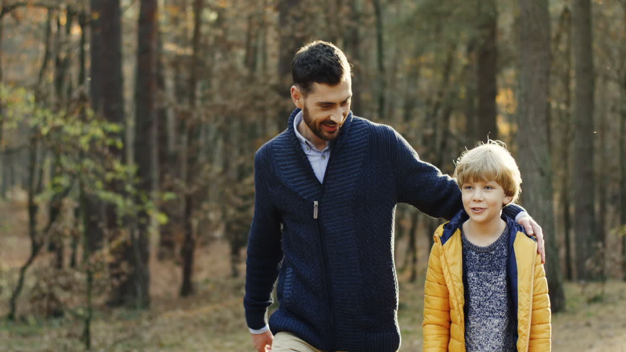 padre feliz caucásico y su pequeño hijo caminando y hablando en el bosque
