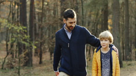 padre feliz caucásico y su pequeño hijo caminando y hablando en el bosque