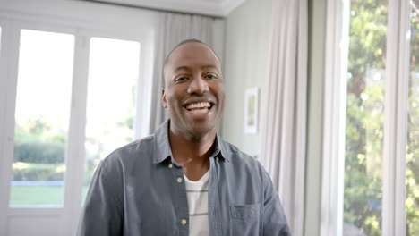 Portrait-of-happy-african-american-man-standing-in-sunny-living-room-smiling,-slow-motion