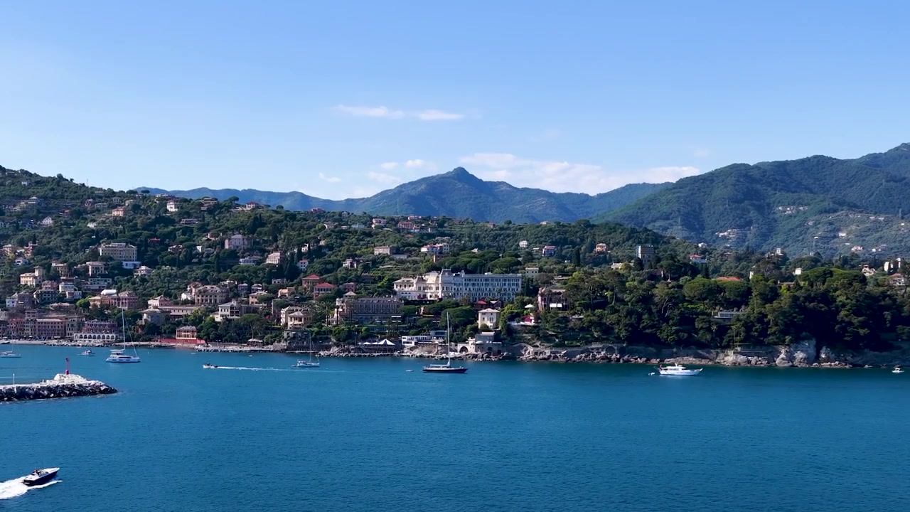 Inquadratura ampia statica di un motoscafo bianco che naviga sull'acqua blu vicino a una città costiera.