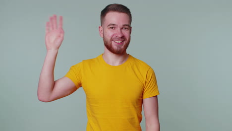 Bearded-man-smiling-friendly-at-camera-and-waving-hands-gesturing-hello-or-goodbye,-welcoming