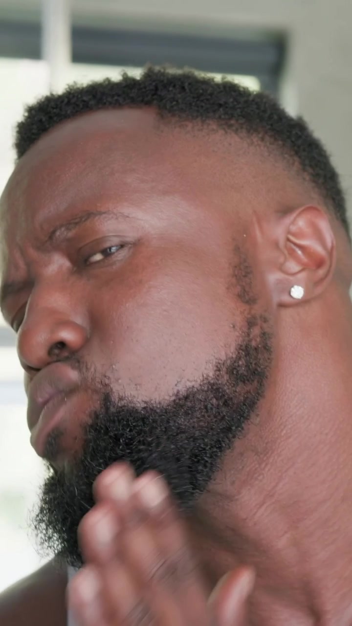 Vertical video: Pressing chin man checking beard by window faucet grey tank ear stud, copy space