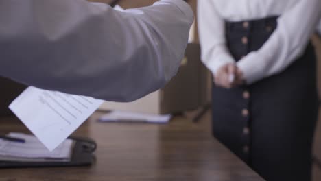 a woman is handling a quitting letter to her boss. he signs it. she carries her things in a box