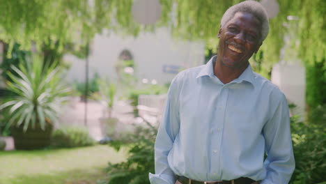 Portrait-Of-Relaxed-Senior-Man-Standing-In-Garden-At-Home-After-Retirement