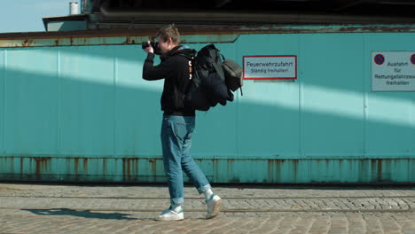 joven fotógrafo con mochila se detiene para tomar una foto de algo