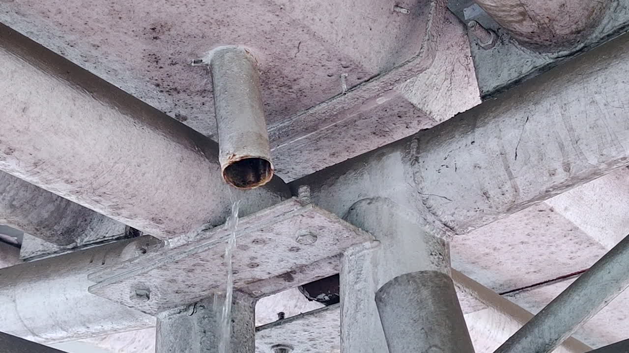 Water leaking from roof pipe inside building structure showing construction defect, drainage issue, maintenance problem, infrastructure damage, and urban building condition