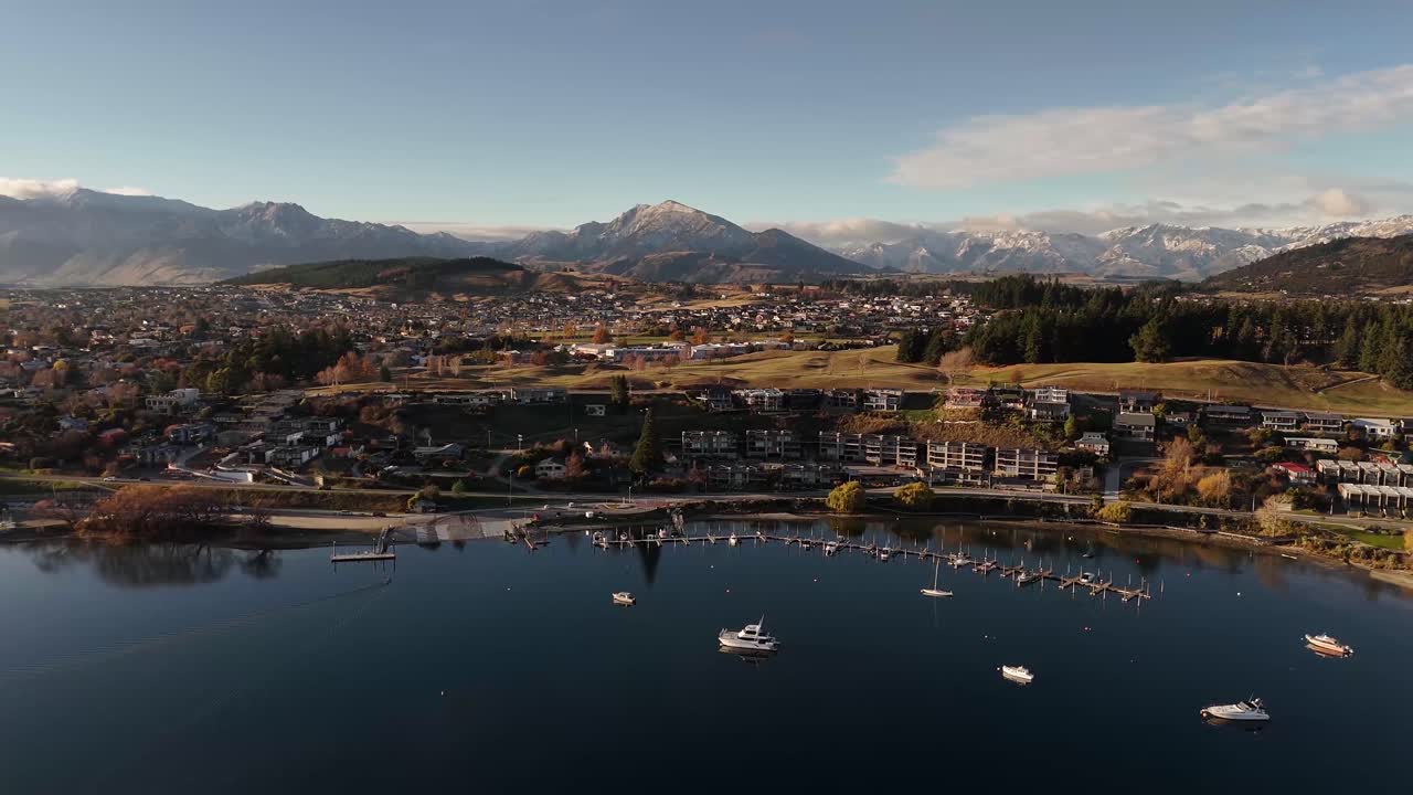 Aerial footage capturing Wanaka Town at sunset, with boats docked along the shore of Wanaka lake in New Zealand
