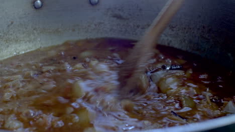 wooden spatula stirring simmering curry sauce with onions-1