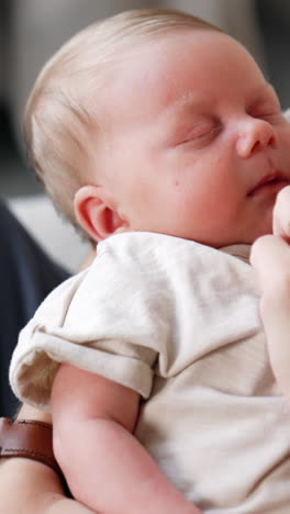 cropped image of a mom holding her sleeping baby in hands. mother touches her child's nose with a finger. close up.. vertical video