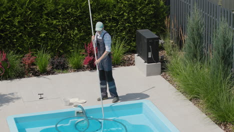 a worker in uniform cleans the pool with a vacuum cleaner, removes dirt from the bottom. tilt shot