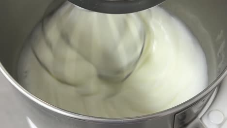 electric mixer mixing egg white and sugar until it is glossy peak and stiff peak, preparing meringue buttercream, commercial kitchen setting close up shot