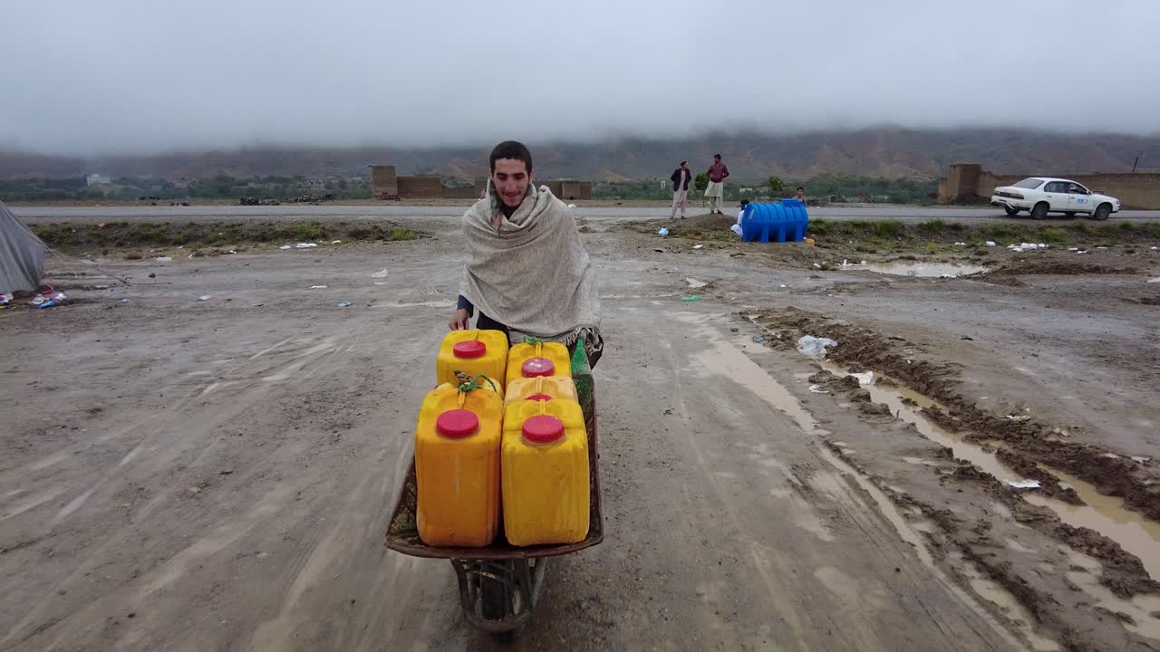 Di Distrik Khwakhe, Provinsi Logar, seorang anak laki-laki membawa air dengan gerobak dorong dalam jeriken di sebuah kamp tempat keluarga berlindung setelah banjir dahsyat memaksa mereka meninggalkan rumah