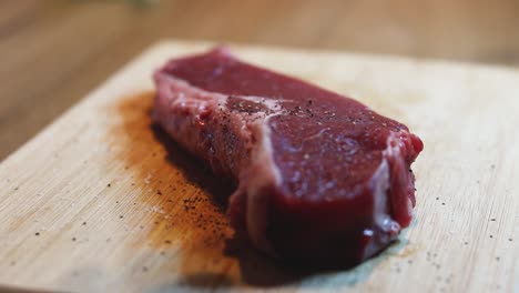 a home chef seasons a thick beef steak with freshly ground pepper on a wooden cutting board, preparing it for cooking on the kitchen counter.