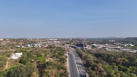 aerial view of a highway winding through a landscape of industry, green hills, and clear skies, showcasing development and nature