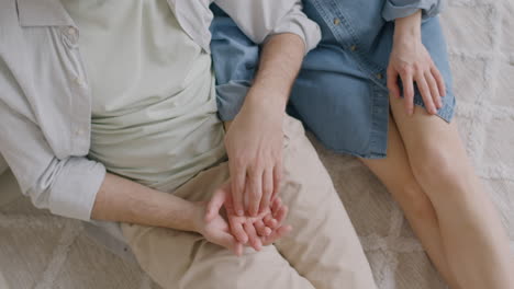 unrecognizable man tenderly touching his girlfriend's hand while sitting together on a carpet at home