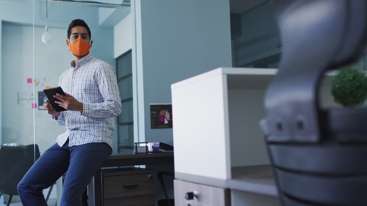retrato de un hombre de oriente medio con una máscara facial usando una tableta digital en una oficina moderna