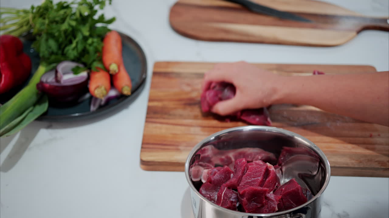 Close up of a woman putting cut up raw beef in a pot in the kitchen