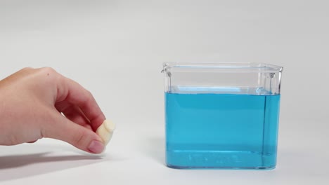 a hand drops a small object into blue liquid, observing its buoyancy and movement in a clear container