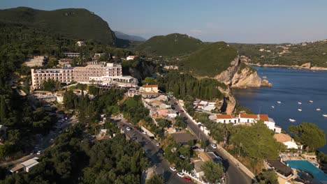 panoramic aerial dolly above cars driving hairpin turn rising to luxury hotel and green mountains of corfu greece