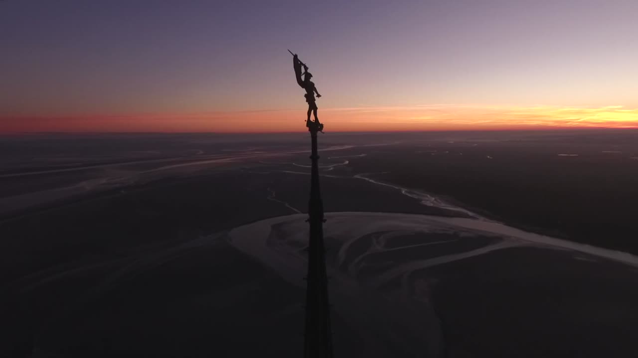 silueta de la estatua en la parte superior de la aguja de la abadía y vista de la bahía al anochecer, mont saint-michel en normandía, francia