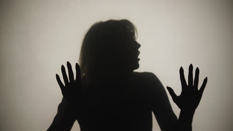 silhouette of woman emerges from smoke and touches glass with her palms