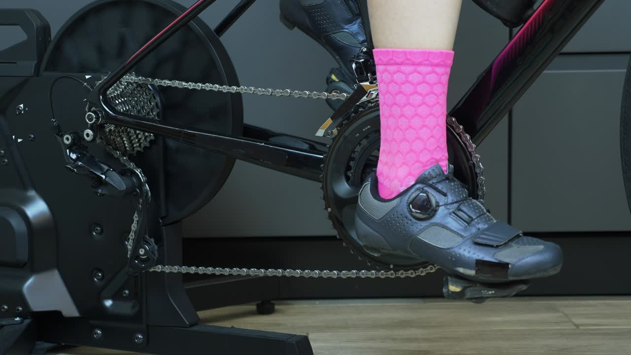 vista de cerca de los pedales de la cadena de la cadena y las piernas ciclando en interiores en una bicicleta estacionaria. sistema de engranajes de la bicicleta de carretera. cassette de bicicleta girando con la cadena y cambiando de marcha. concepto de ciclismo