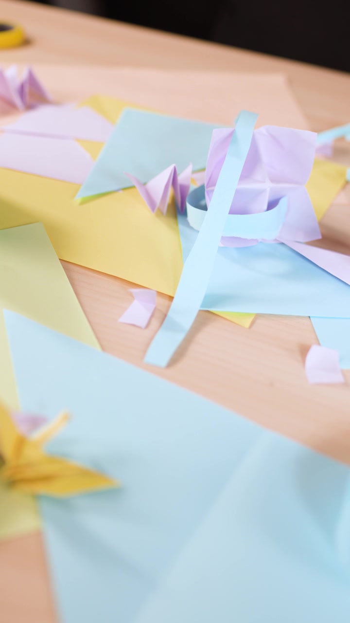 Un primo piano statico cattura varie forme di origami color pastello e scarti di carta su una scrivania.