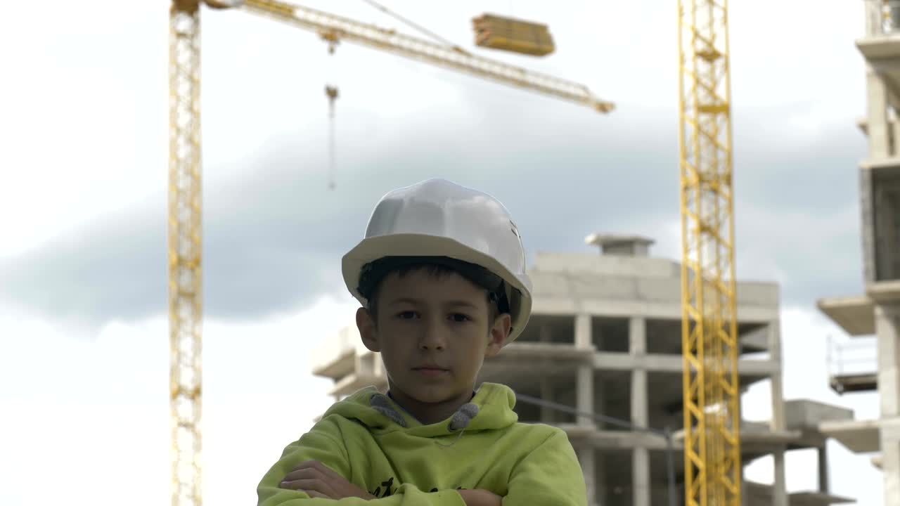 niño constructor se encuentra entre grúas constructoras y mira a la cámara, niño juega a un constructor