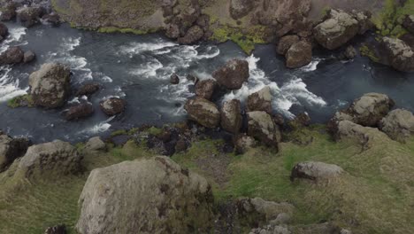 Toma-Aérea-De-Drones-En-Ascenso-De-Un-Hermoso-Río-Y-Rápidos-En-Islandia-En-Un-Día-Oscuro-Y-Brumoso-Frente-A-Los-Acantilados-Y-Rocas-Verdes-Y-Cubiertos-De-Musgo