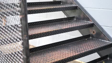 Rain-falling-on-industrial-metal-stairs-as-a-man-runs-up-them-wearing-work-out-athletic-clothes-in-slow-motion