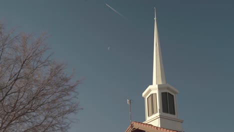 mormon church spire with moon and plane leaving chem trails and contrails behind 4k