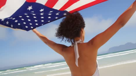 woman standing by the sea with a waving american flag.at beach 4k