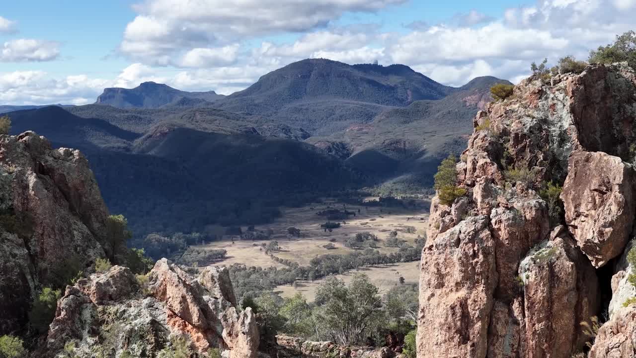 Una ripresa panoramica su scogliere frastagliate rivela una profonda valle e catene montuose distanti.