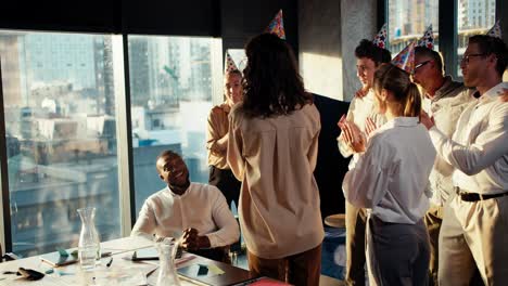 congratulation black male businessman in a business team at work in the office. colleagues in festive hats brought a cake with