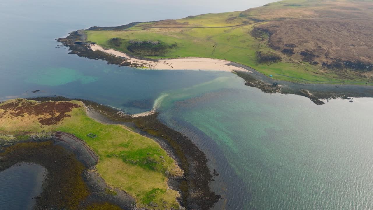 Aerial drone shot of Coral Beach on the Isle of Skye, Scotland, with turquoise waters, white sand, and surrounding green hills creating a stunning coastal landscape