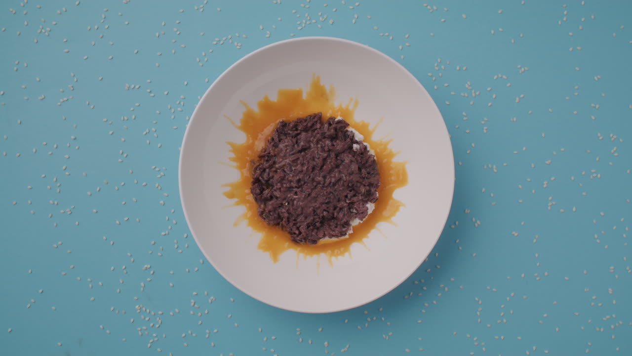 Preparing a dish of dark purple rice with orange sauce and sesame seeds