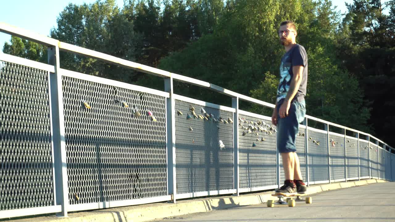 Giovane che pattina con il longboard su un ponte con lucchetti, divertendosi.
