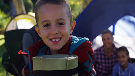 Boy-holding-a-rolled-mat-while-family-sitting-in-the-tent