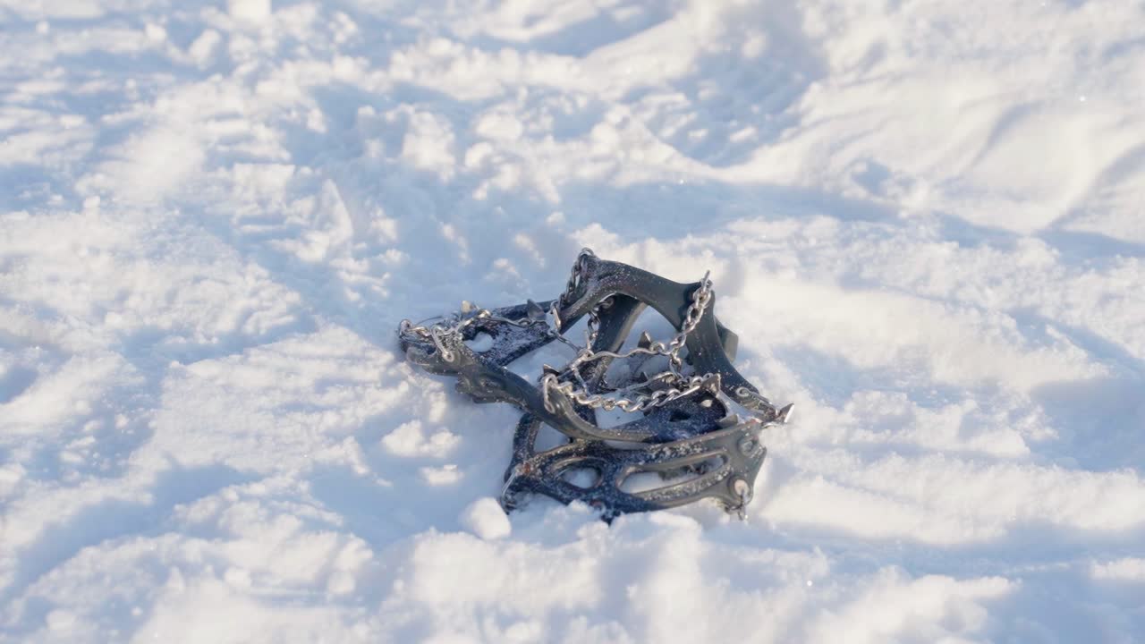 Pair of snow spikes to attach to shoes for better traction drops onto snow, slow motion.