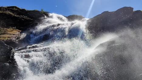 powerful splashing waterful in beautiful sunlight at vikafjell mountain in norway - spring with blue sky and camera almost inside the lower part of waterfall - low angle looking up at waterfall