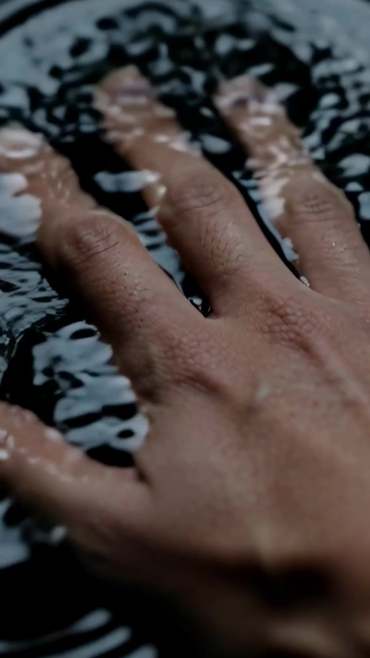 Vertical video: Touching right hand pressing fingertips into dark water, creating ripple patterns