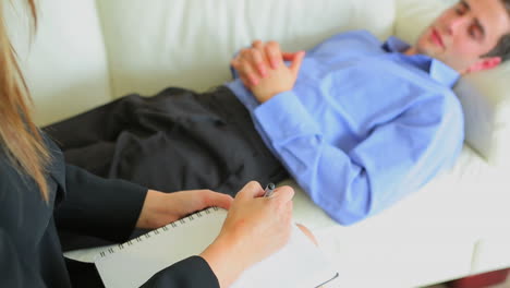 terapeuta tomando notas mientras el paciente yace en el sofá