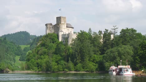 niedzica castle in poland over the mountain with the lake under it and tourist ferrys