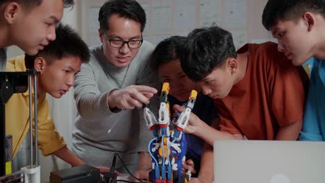 asian man with a laptop and 3d printing teaching the boys repairing a cyborg hand at school