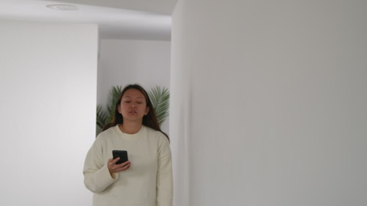 Donna stressata o ansiosa seduta per terra, appoggiata al muro a casa, che reagisce a notizie, messaggi o storie di internet o social media sul telefono cellulare 4