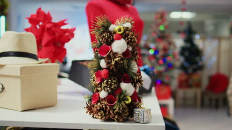 primer plano de un árbol de navidad festivo en miniatura elaborado con piñas sentado en la mesa de exhibición de una tienda de ropa junto a elegantes corbatas. decoración navideña en una tienda de moda vacía